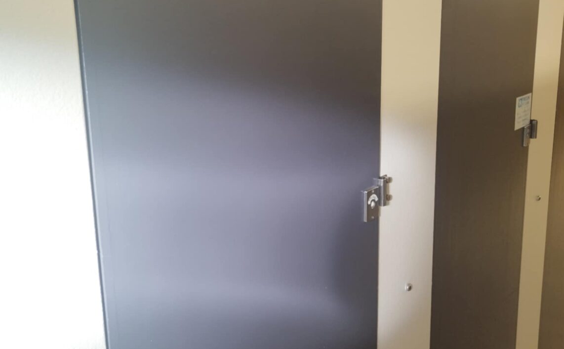 A brown door of a public toilet with light reflecting on it.