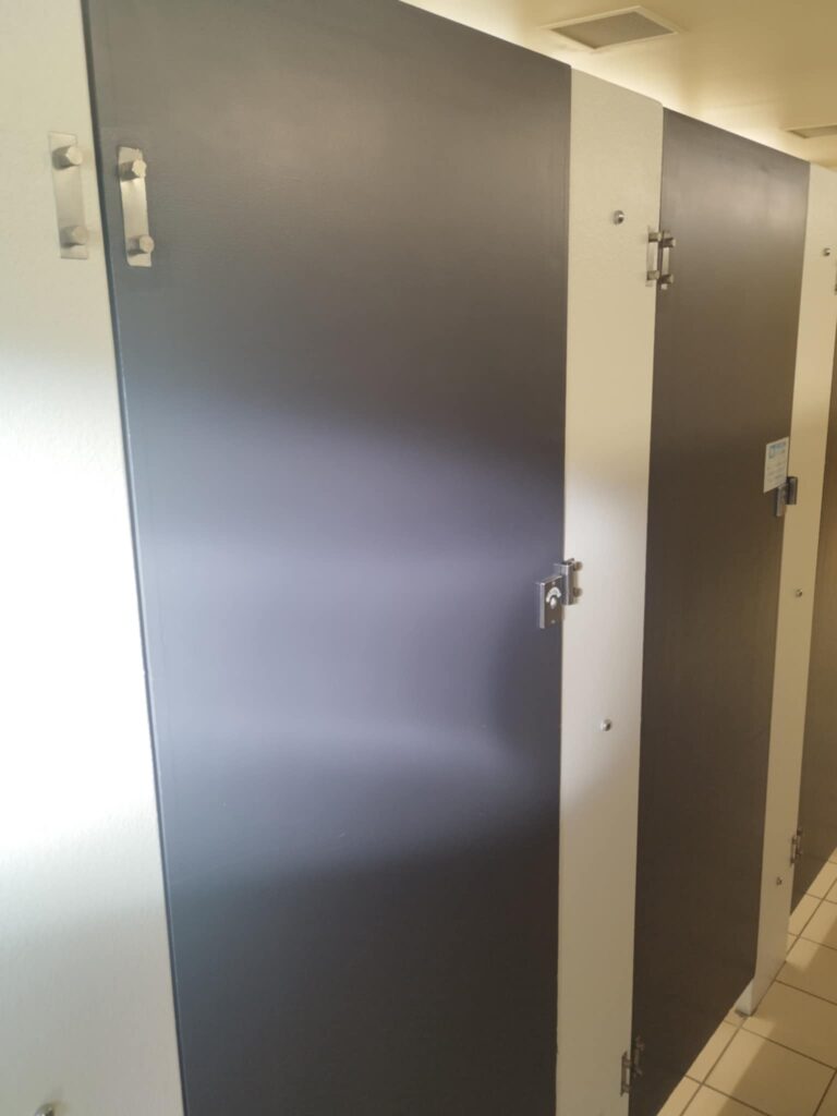 A brown door of a public toilet above tiles with light reflecting on it