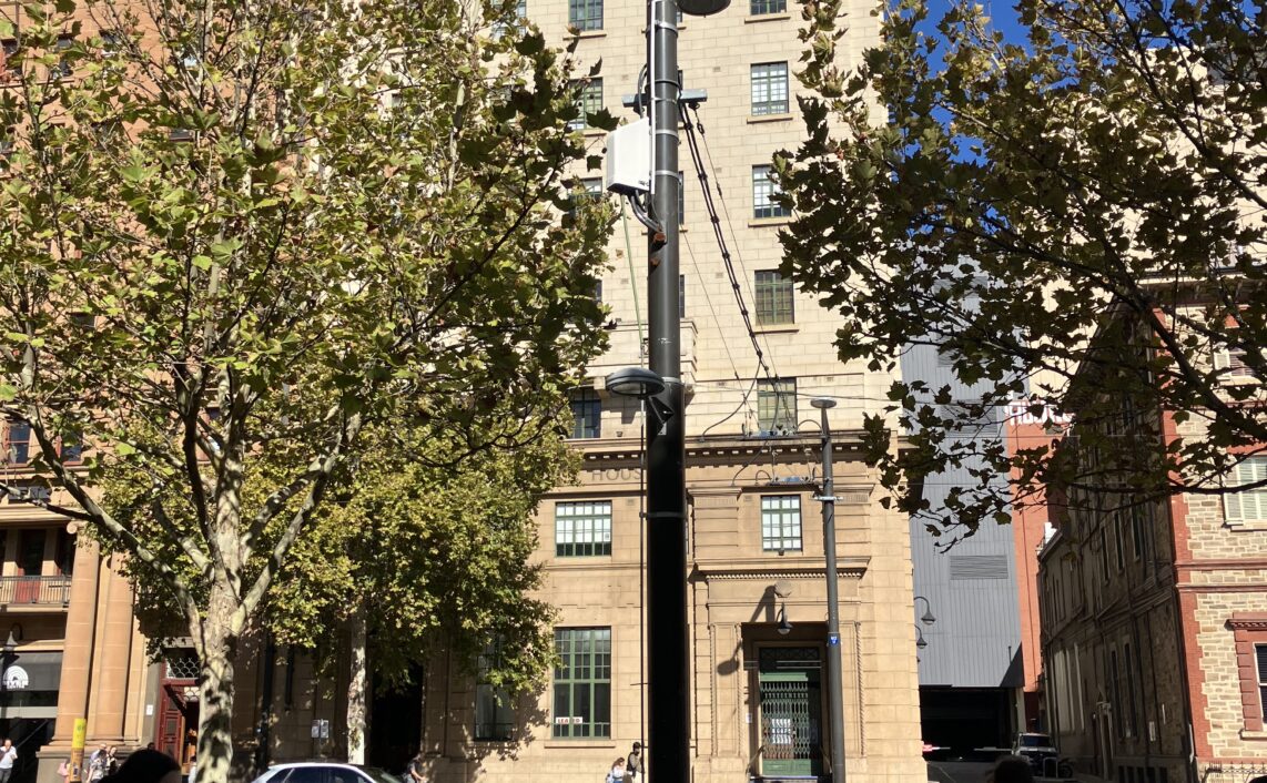 People crossing a street with benches in the foreground and colonial buildings in the background